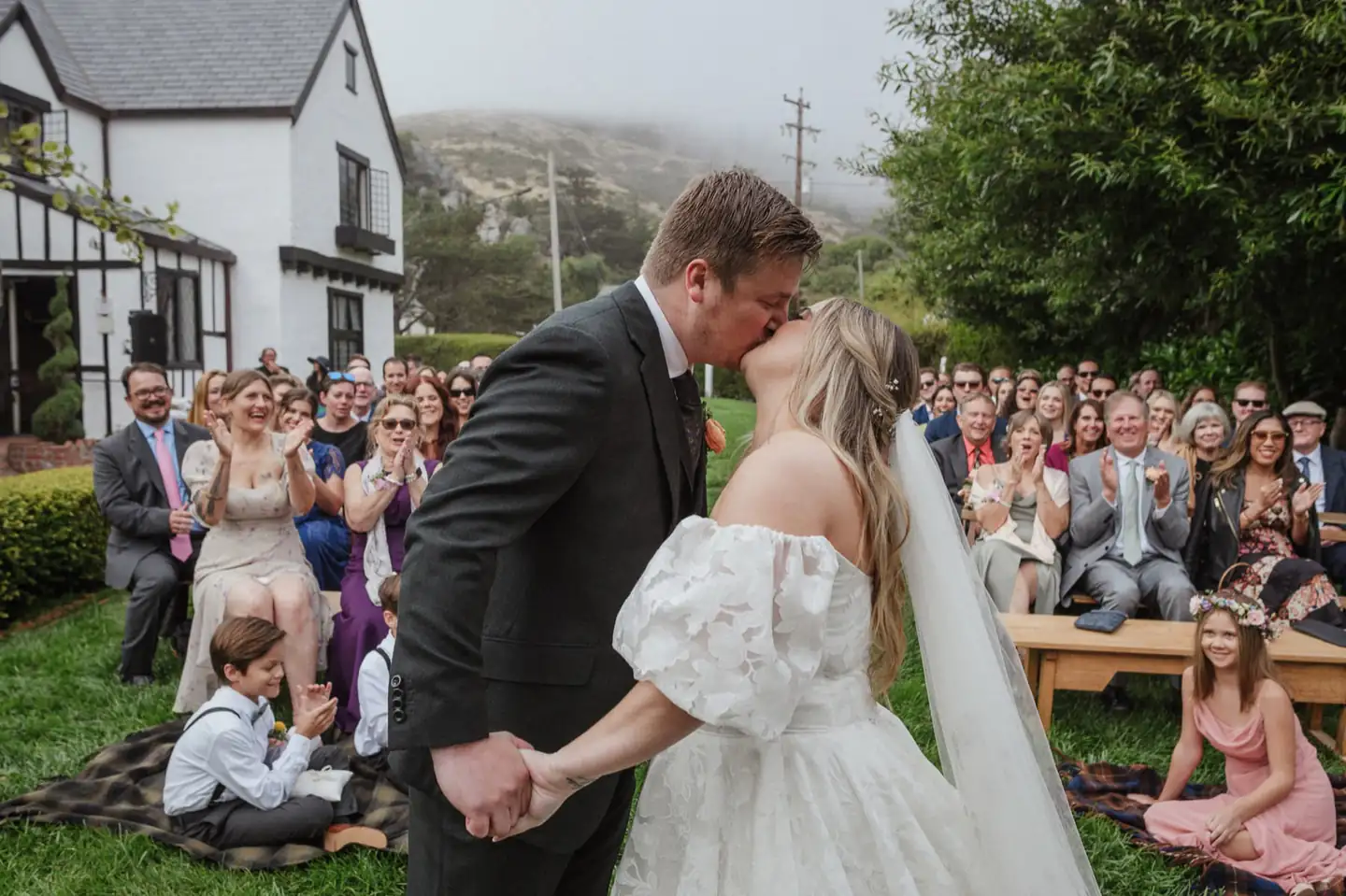 Newlyweds kissing as their wedding guests cheer around them