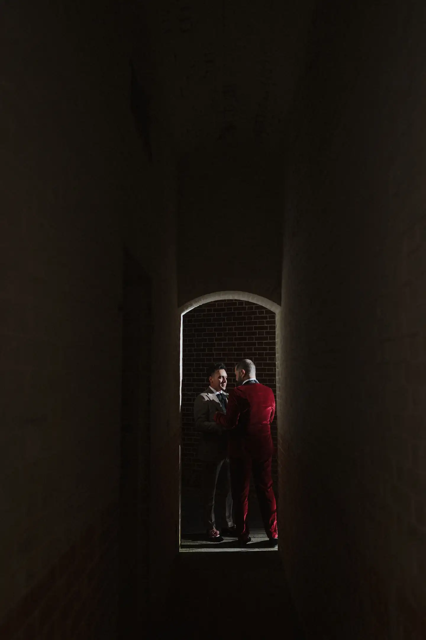 A couple framed in a shaft of light beneath a dark architectural arch