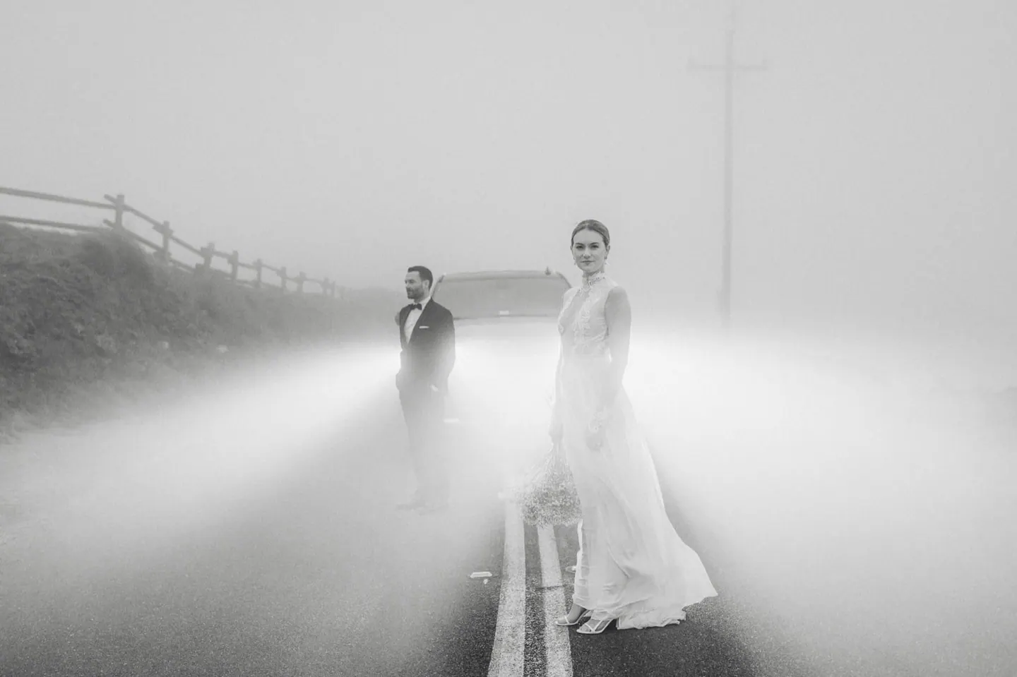A couple standing in fog and car headlights in black and white