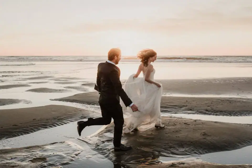 Newlyweds running together across a wide beach