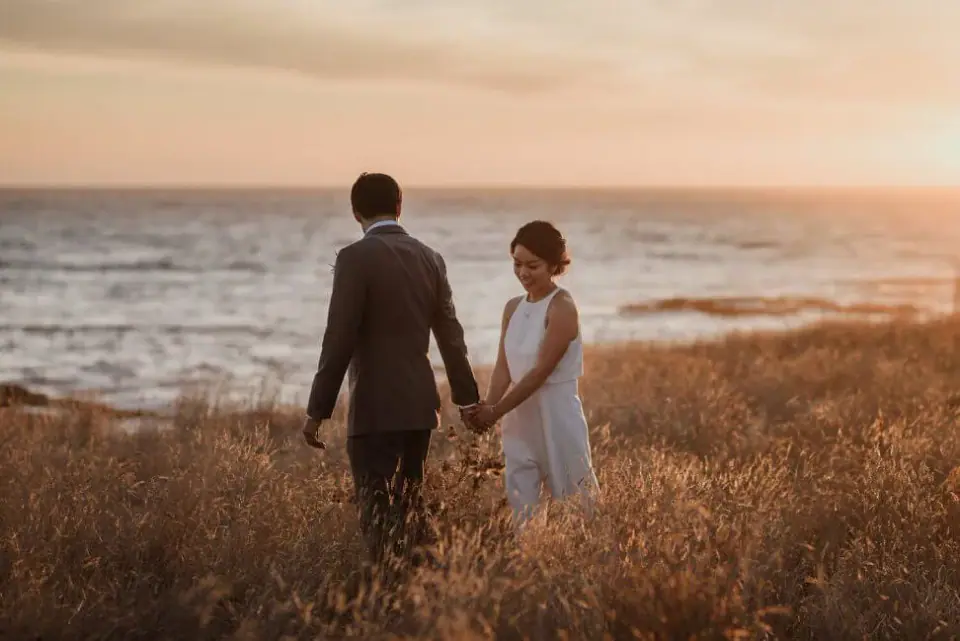 A couple walking together beside the ocean at sunset