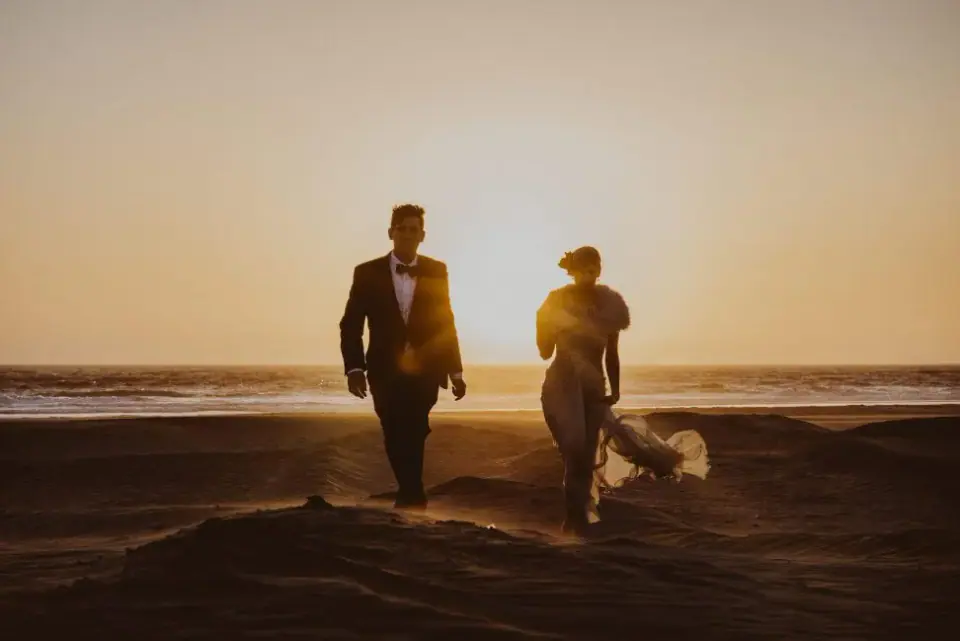 A bride and groom running along the beach at sunset