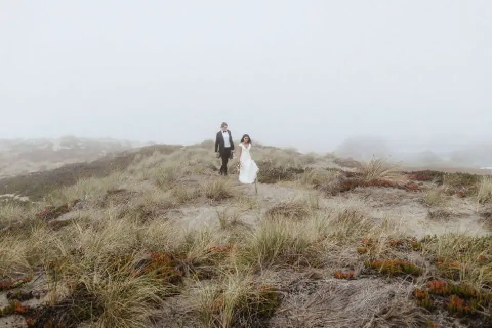 An eloping couple walking through coastal dunes