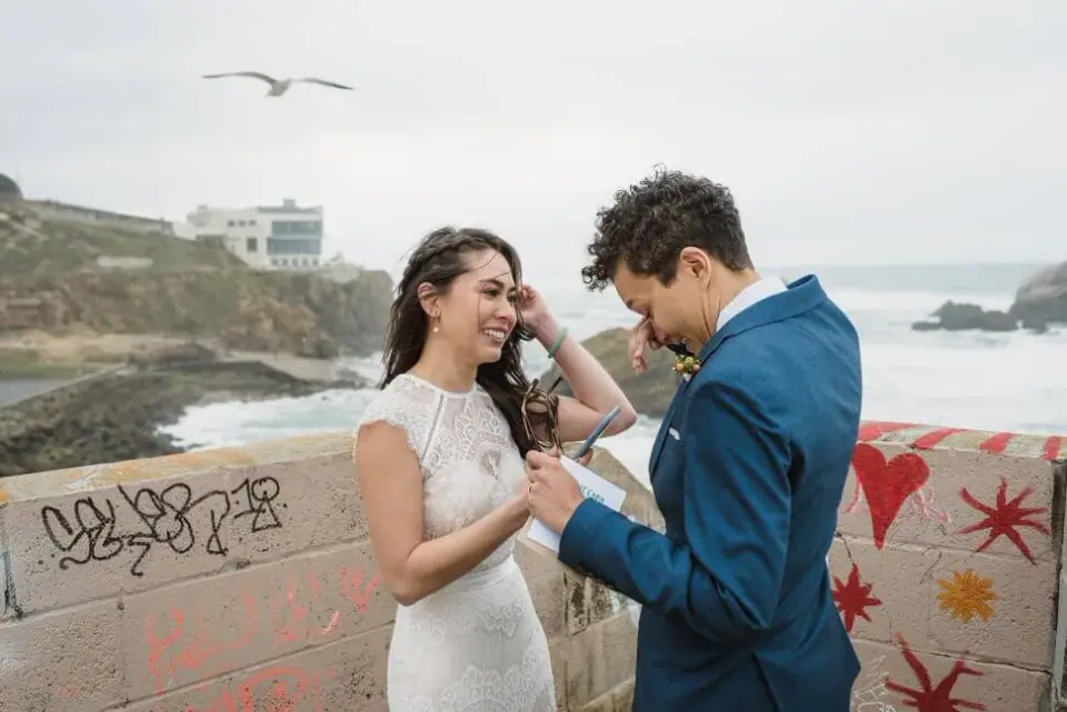 A couple exchanging rings beside bright coastal street art