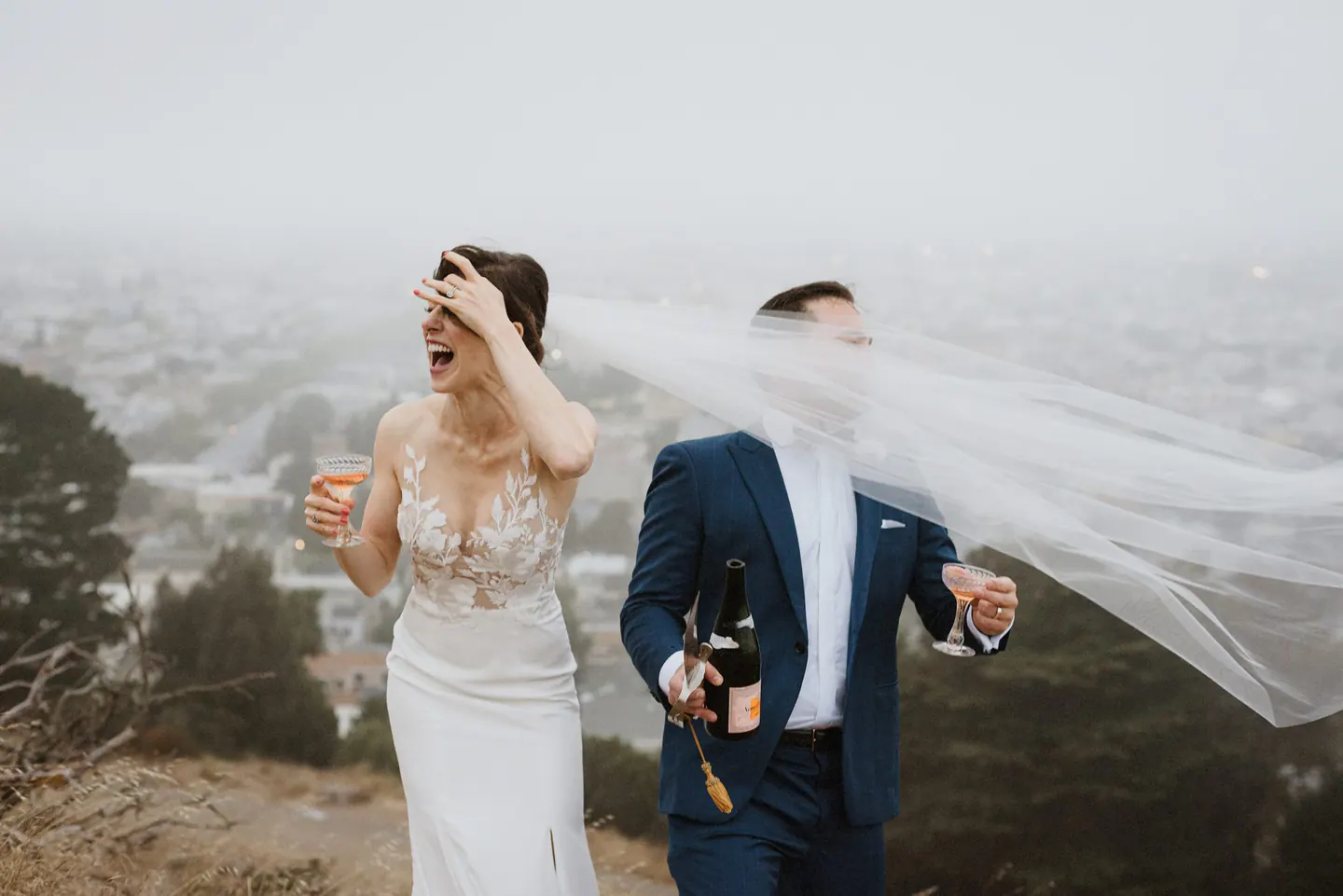 Newlyweds laughing as wind carries a veil across a Marin wedding portrait