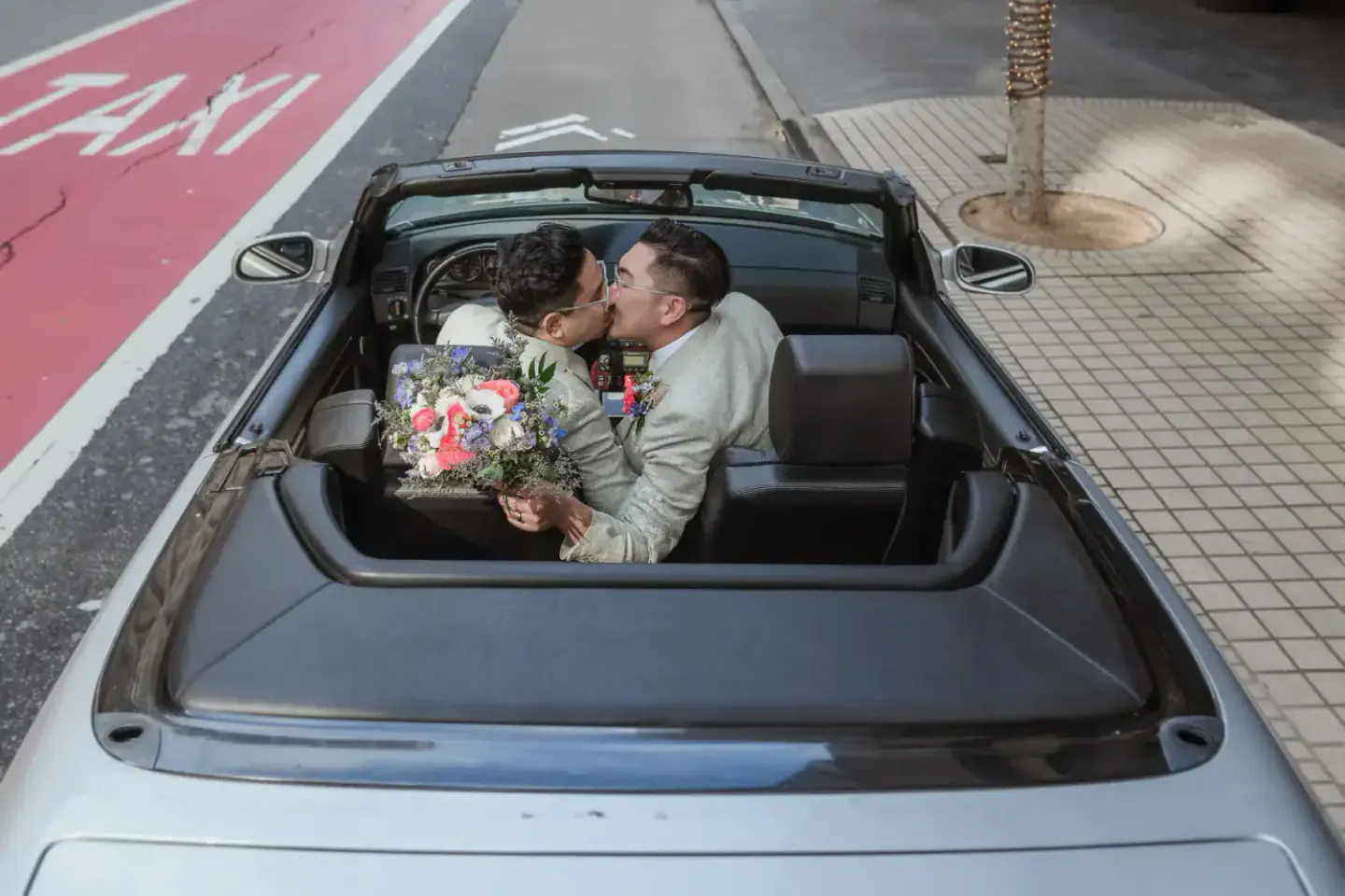 Two grooms celebrating in a convertible after their San Francisco City Hall wedding