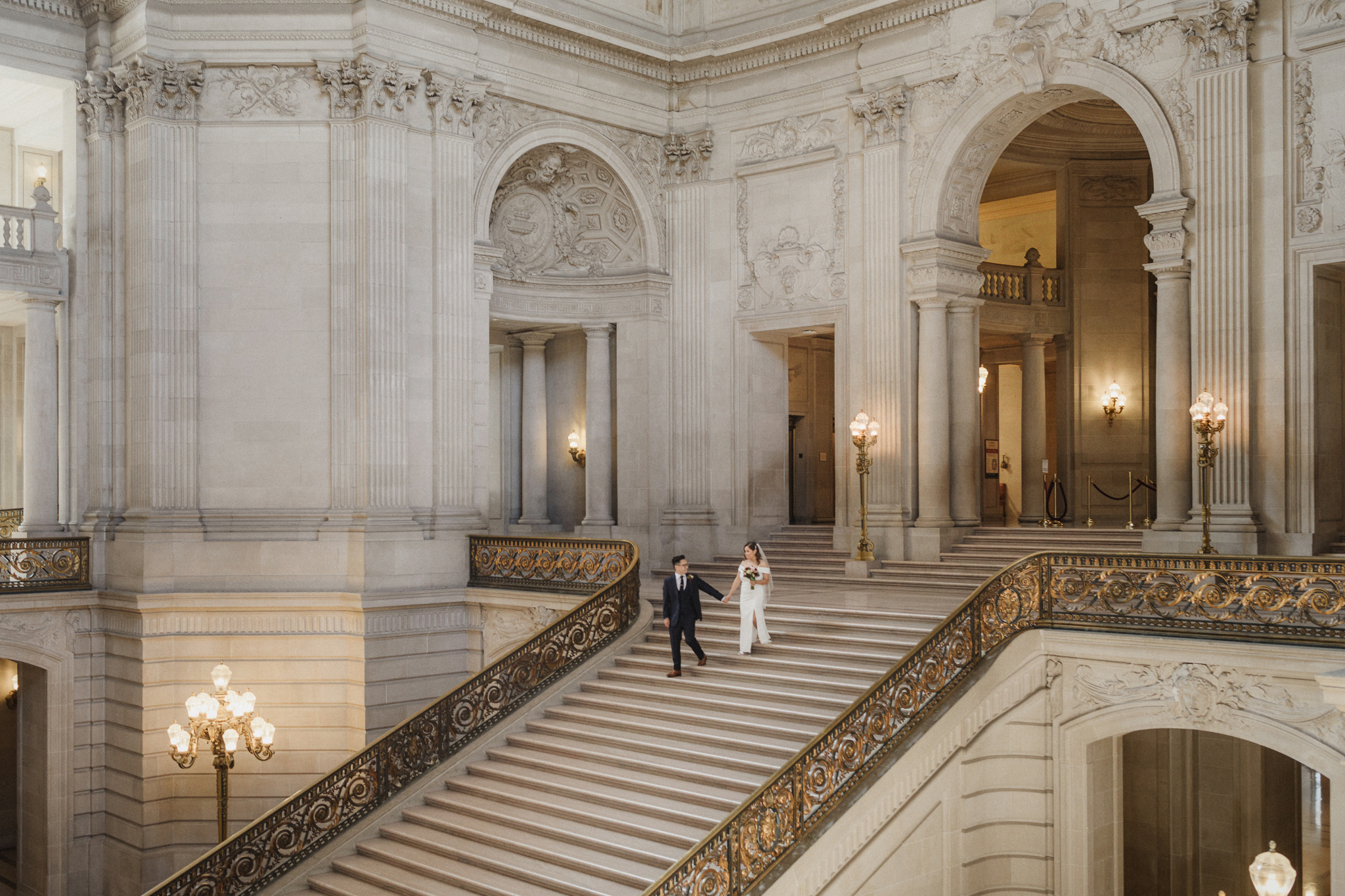 Newlyweds crossing the grand staircase inside San Francisco City Hall