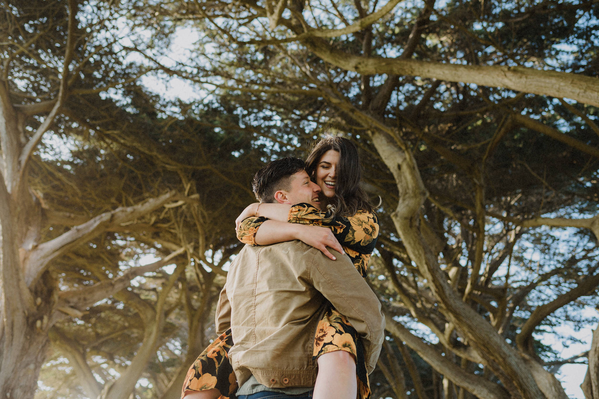 An unposed embrace beneath a windswept coastal tree