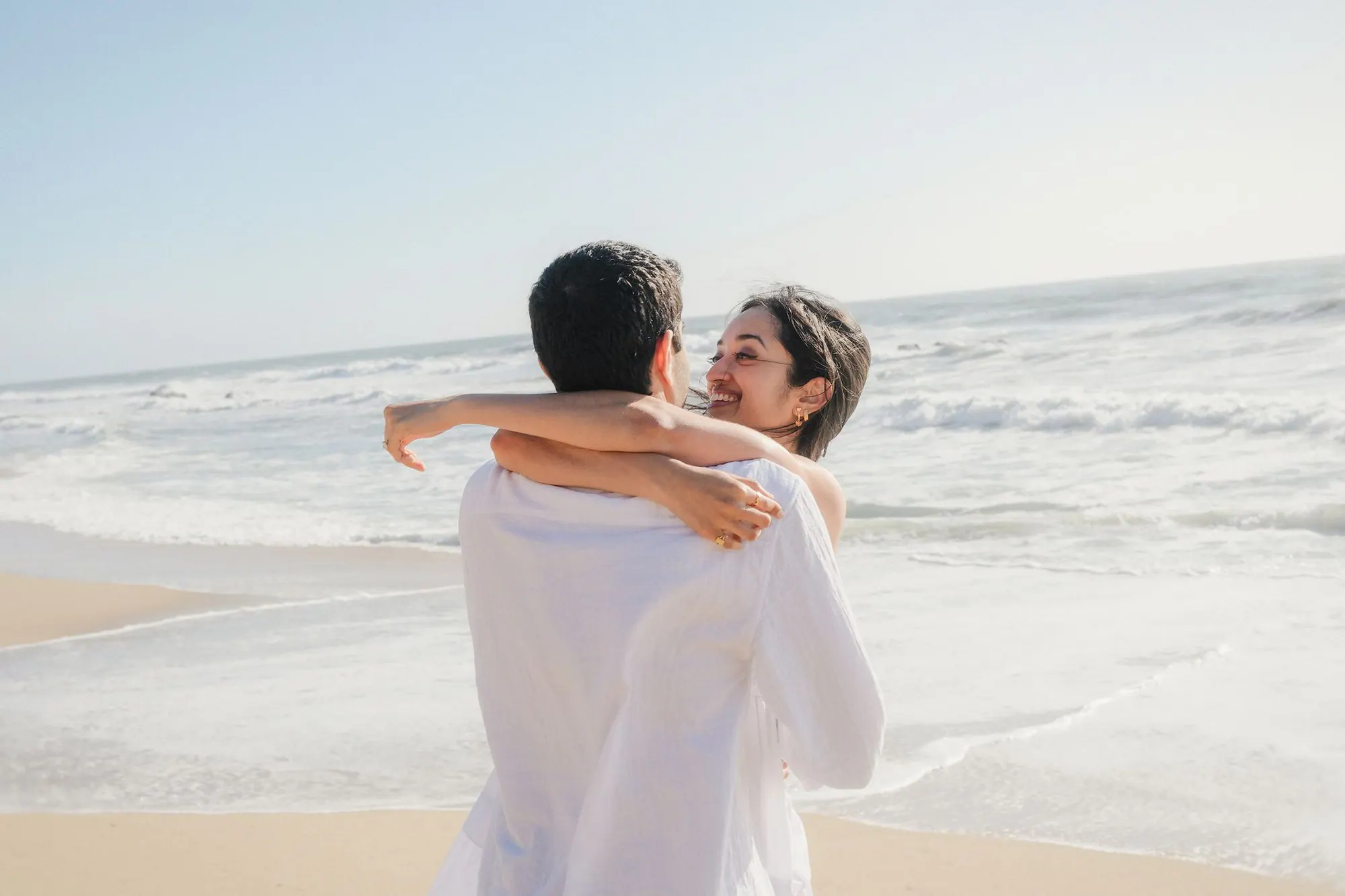 The couple embracing on the beach after their Half Moon Bay proposal